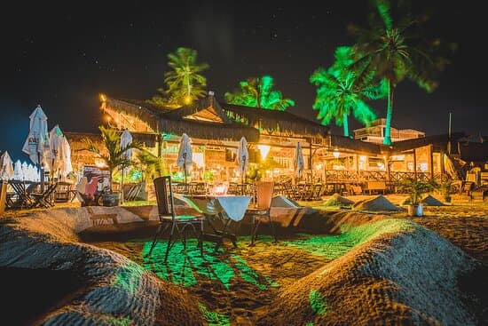 Mesas cavadas na areia em um recanto da praia de Flecheiras iluminado à noite, com coqueiros sob luz verde