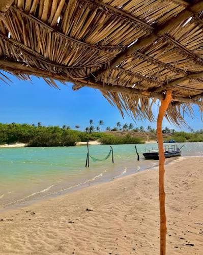 Veduta della spiaggia e del fiume a Cana Brava, con barca da pesca sotto una tettoia di paglia, costa di Trairi, Ceará