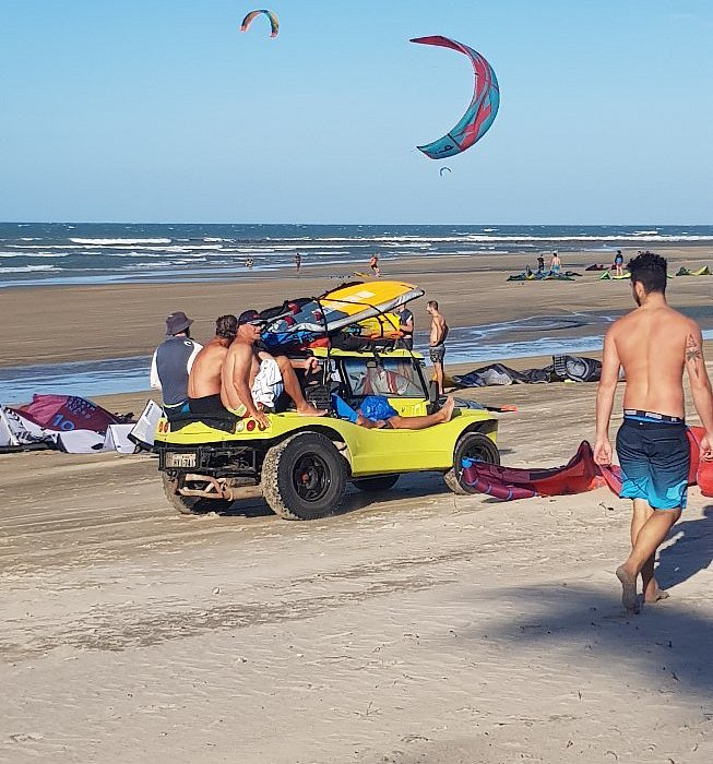 Bugue amarelo parado na praia de Emboaca com kitesurfistas e kites voando ao fundo