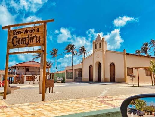 Praça da vila de Guajiru, com placa de boas-vindas e igreja ao fundo