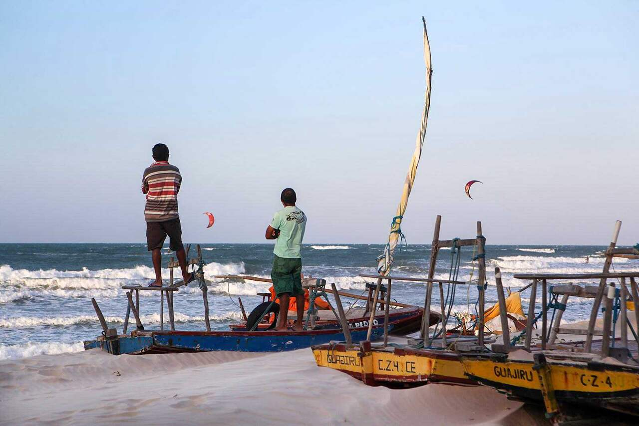 Pescadores ao lado de jangadas na praia de Guajiru, com barco identificado com o nome da vila